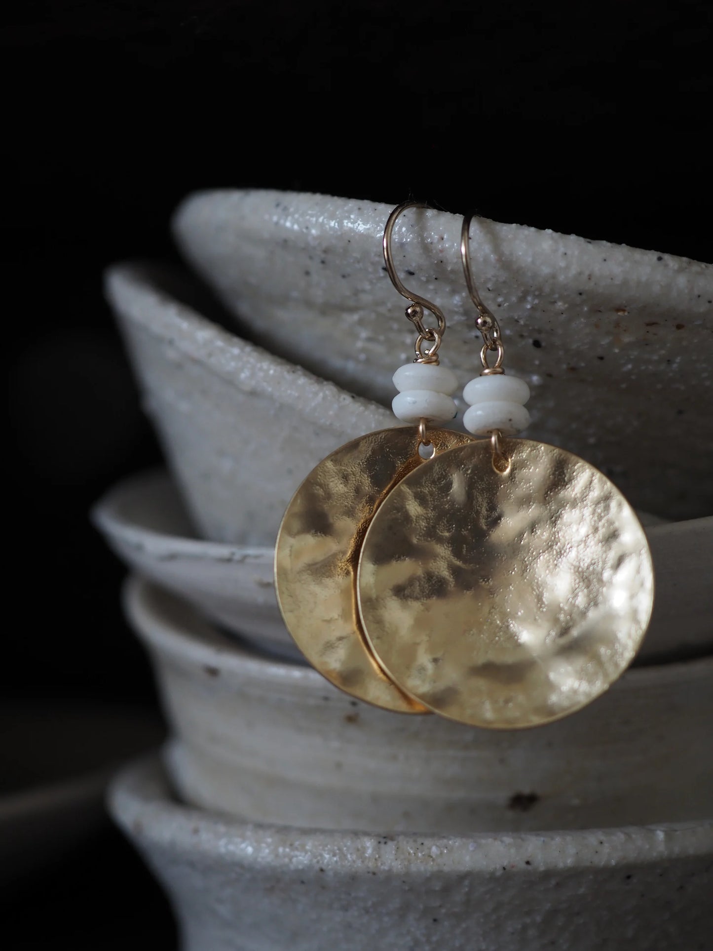 Gold earrings with white beads and circle pendant on a dark background