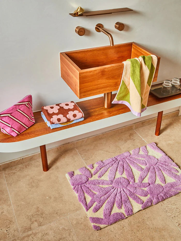 Bathroom with wooden sink, towels, and a purple bath mat on a beige floor.