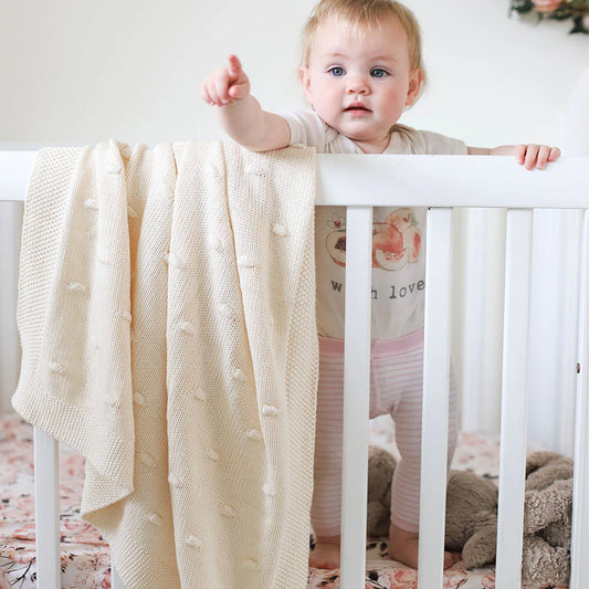 Baby in a crib with a cream-colored blanket