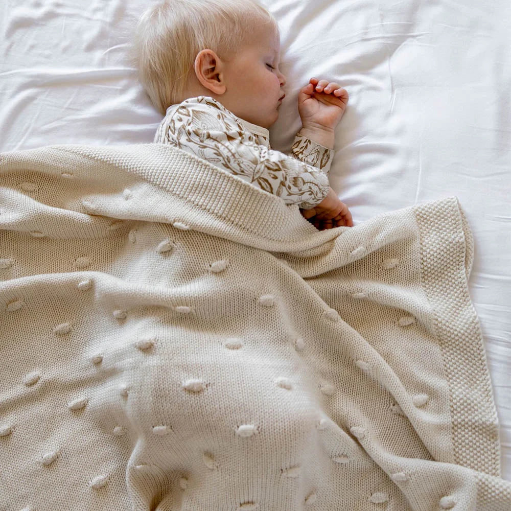 Baby wrapped in a textured blanket on a white bed