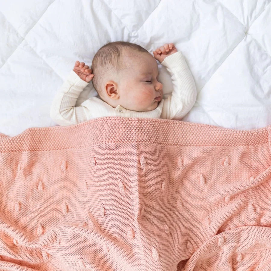 Baby lying on a white surface with a pink textured blanket