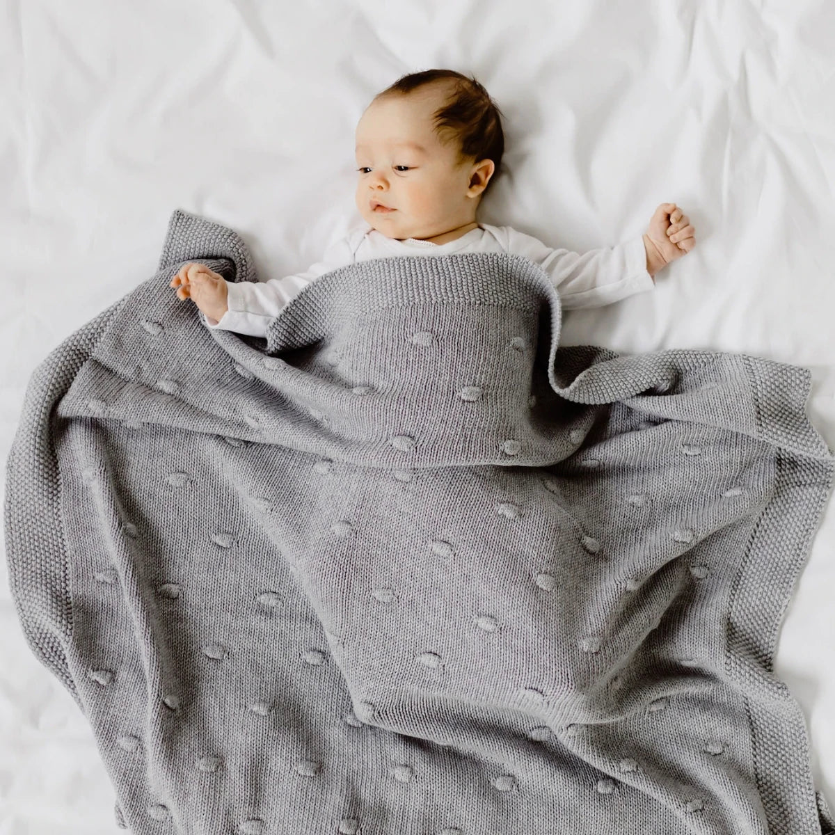 Baby wrapped in a gray polka dot blanket on a white bed