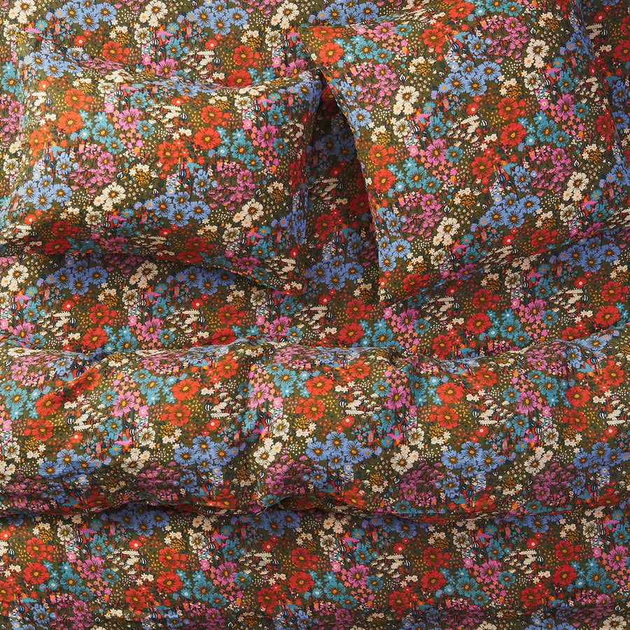 Close-up of colorful floral patterned fabric. Khaki green base colour with flowers in teal, pink, orange/red, white and small orange details.