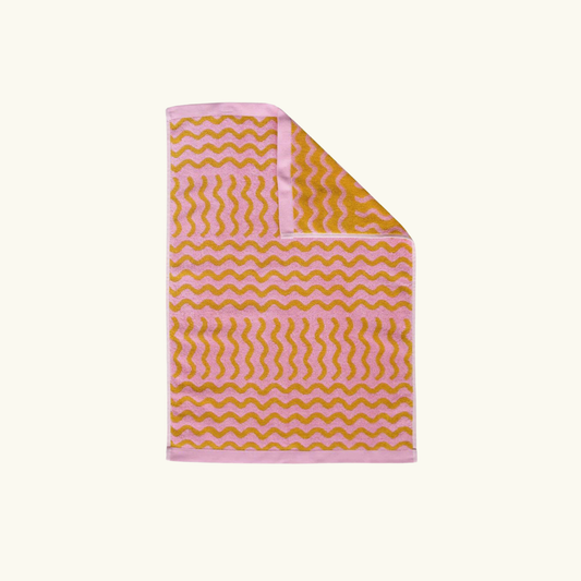 Pink and yellow/mustard wavy patterned hand towel on a white background.