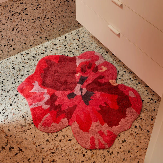 Red floral-patterned bath mat on a speckled floor.