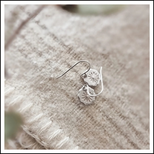 Silver floral earrings on a textured beige fabric background
