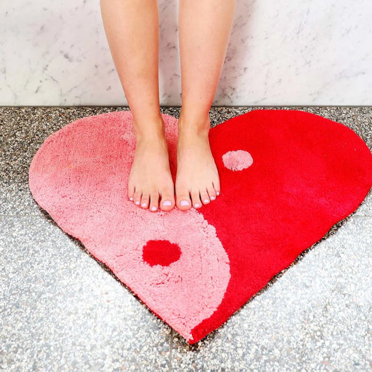 Heart-shaped pink and red rug with a person standing on it.