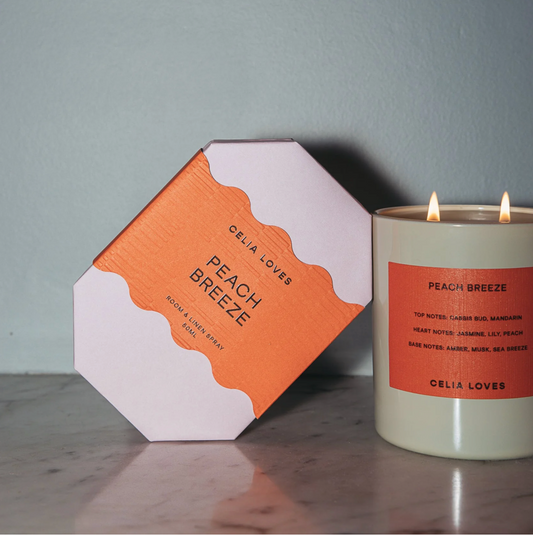 Candle with 'Peach Breeze' packaging on a wooden surface