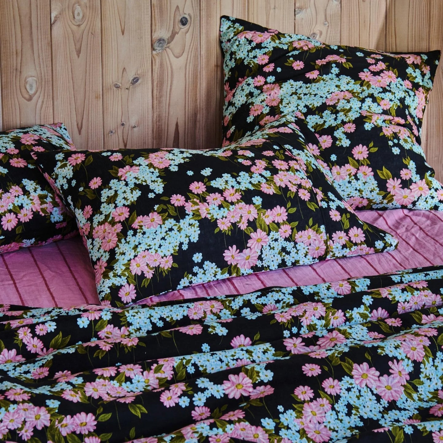 Floral bedding set with pink and blue flowers on a black background, featuring pillows and a quilt on a wooden bed frame.
