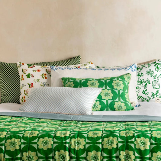 Green floral patterned bedding with various pillows on a bed.