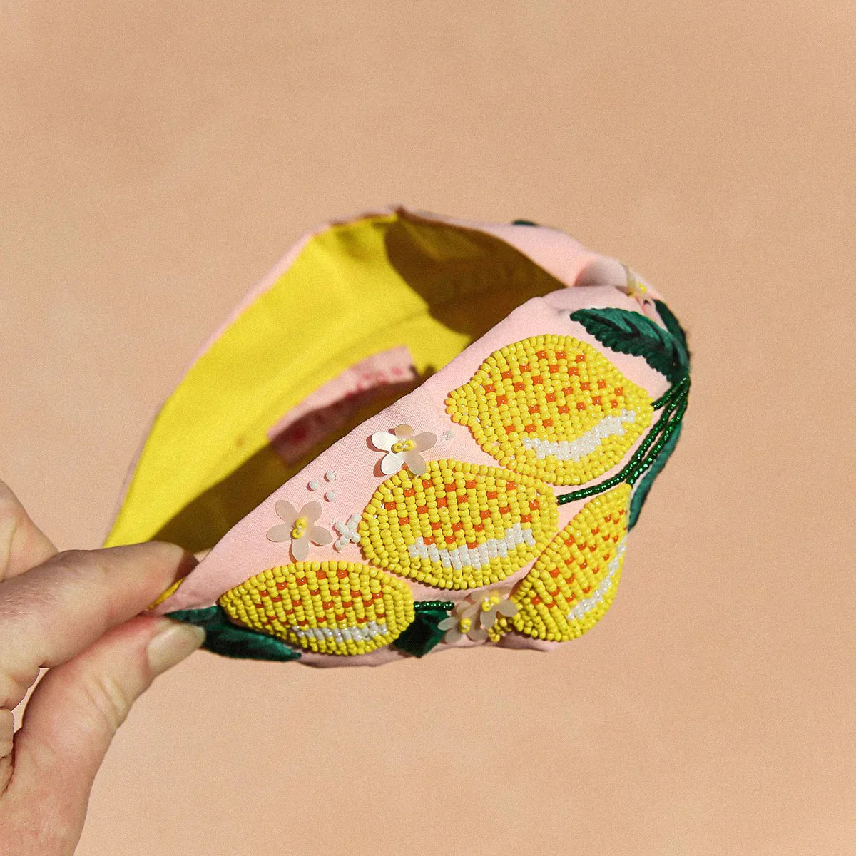 Hand holds base of pink headbang with yellow lemon details and green leaves, with small white flower details. Yellow inside lining and kingston branding.
