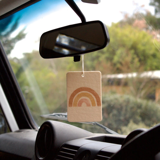 Car air freshener with rainbow design hanging from a car's rearview mirror.