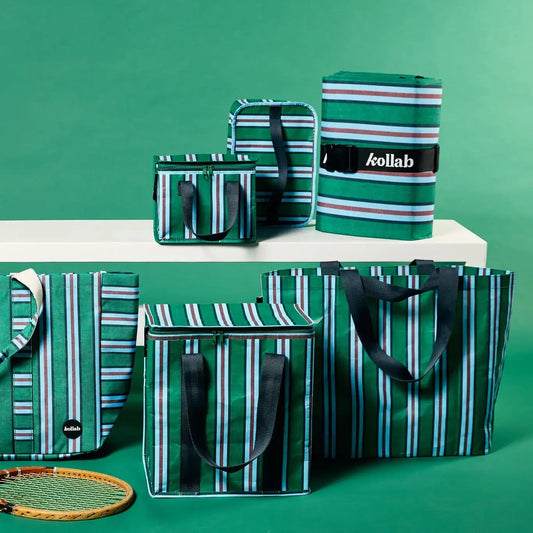 A coordinated set of green striped Kollab bags and a matching rolled bag, displayed on a white platform against a green studio background. The set includes tote bags, cooler-style bags, and a rolled travel bag, all with black handles and a black brand label.