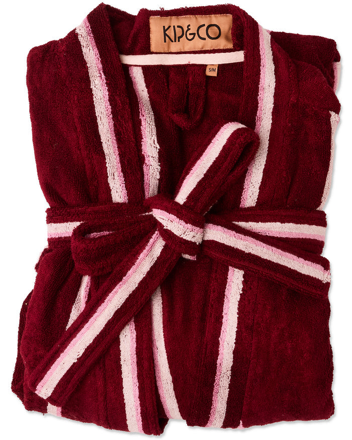 A folded maroon plush bathrobe with white and light pink striped borders and a matching tie belt, shown on a plain white background. The brand label inside the collar reads KIP&CO.