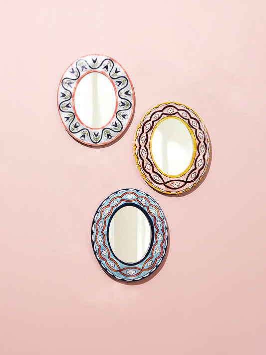 Three decorative oval mirrors with colorful frames on a pink background