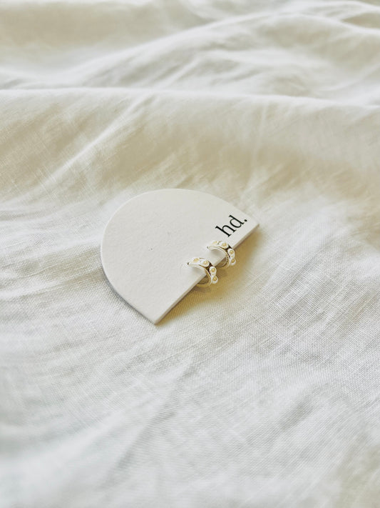 Silver hoop earring with three small pearl details embedded in silver. Products sits on hd white arch card, sitting on white linen background.
