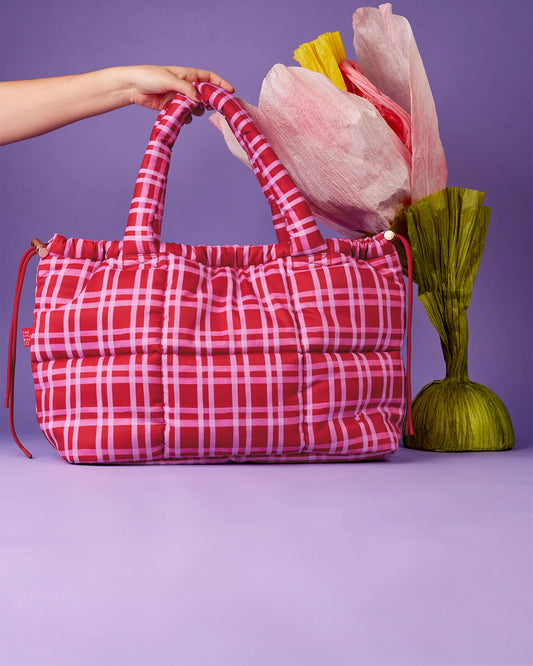 Red plaid bag held by a hand with decorative flowers on a purple background