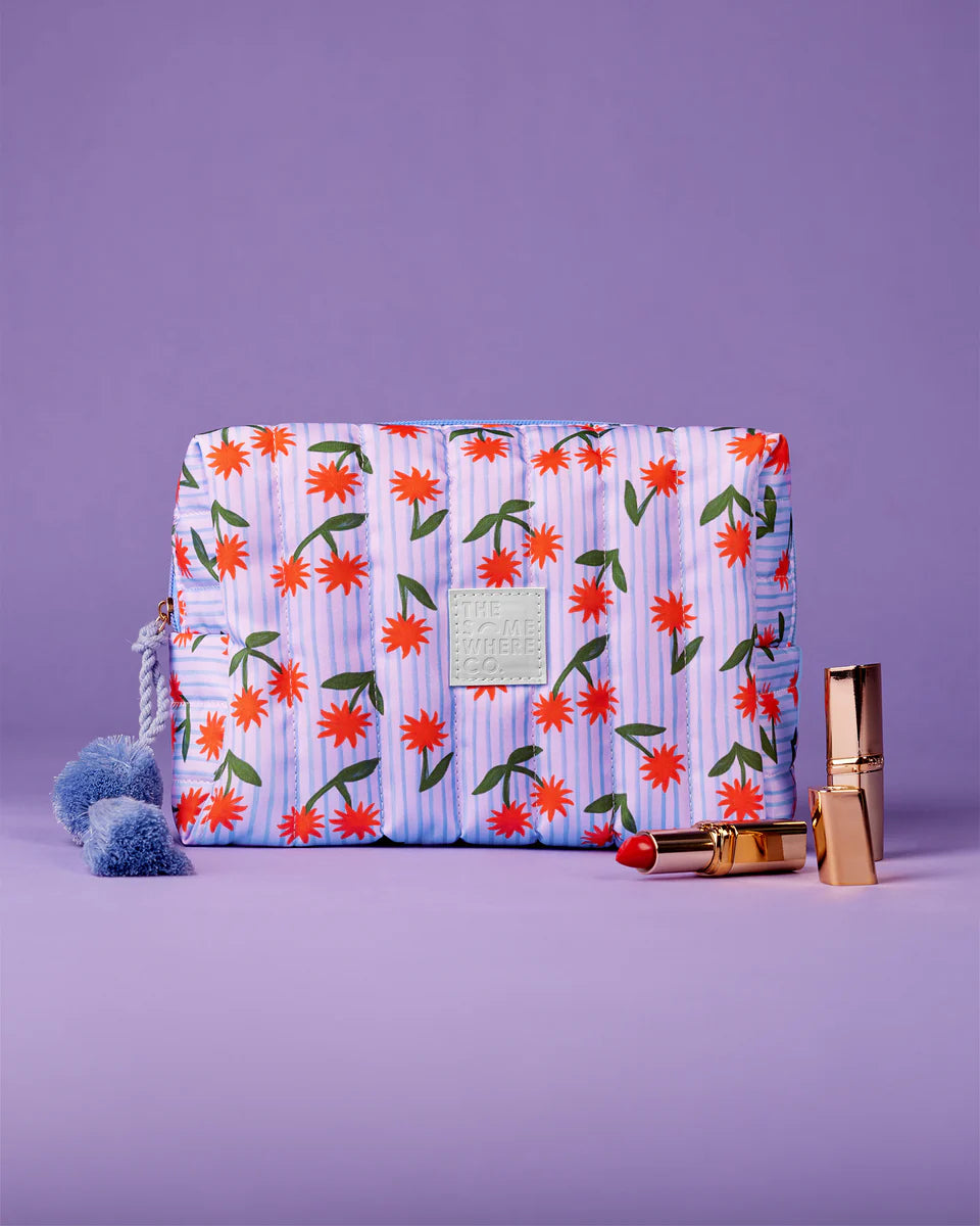 Floral-patterned clutch bag with pom-pom details on a purple background