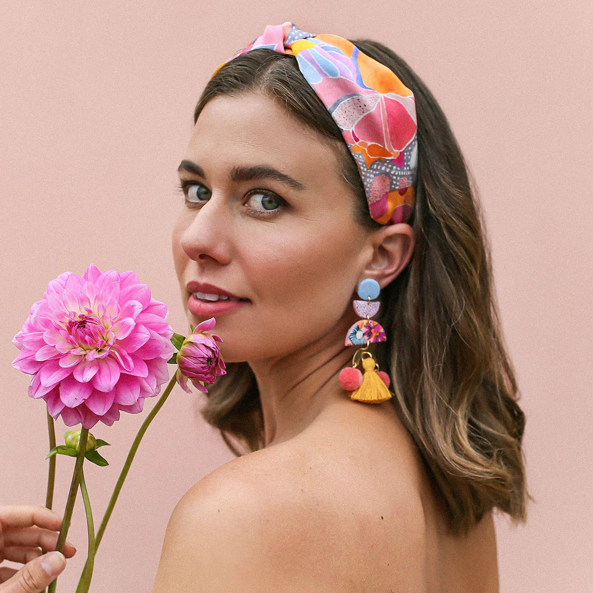 Woman wears silk headband, matching clay earrings and holding a pink flower.