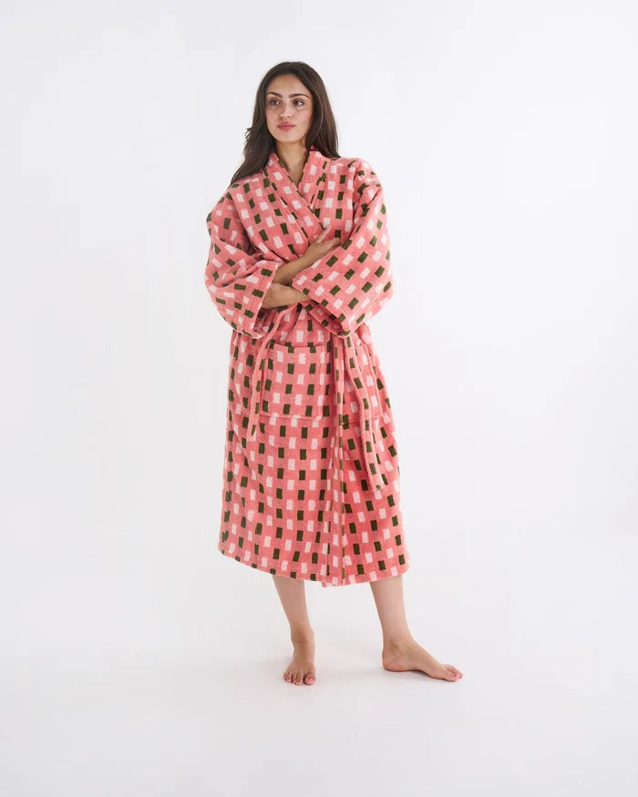 A woman modeling a pink and black checkered bathrobe against a plain white studio background.