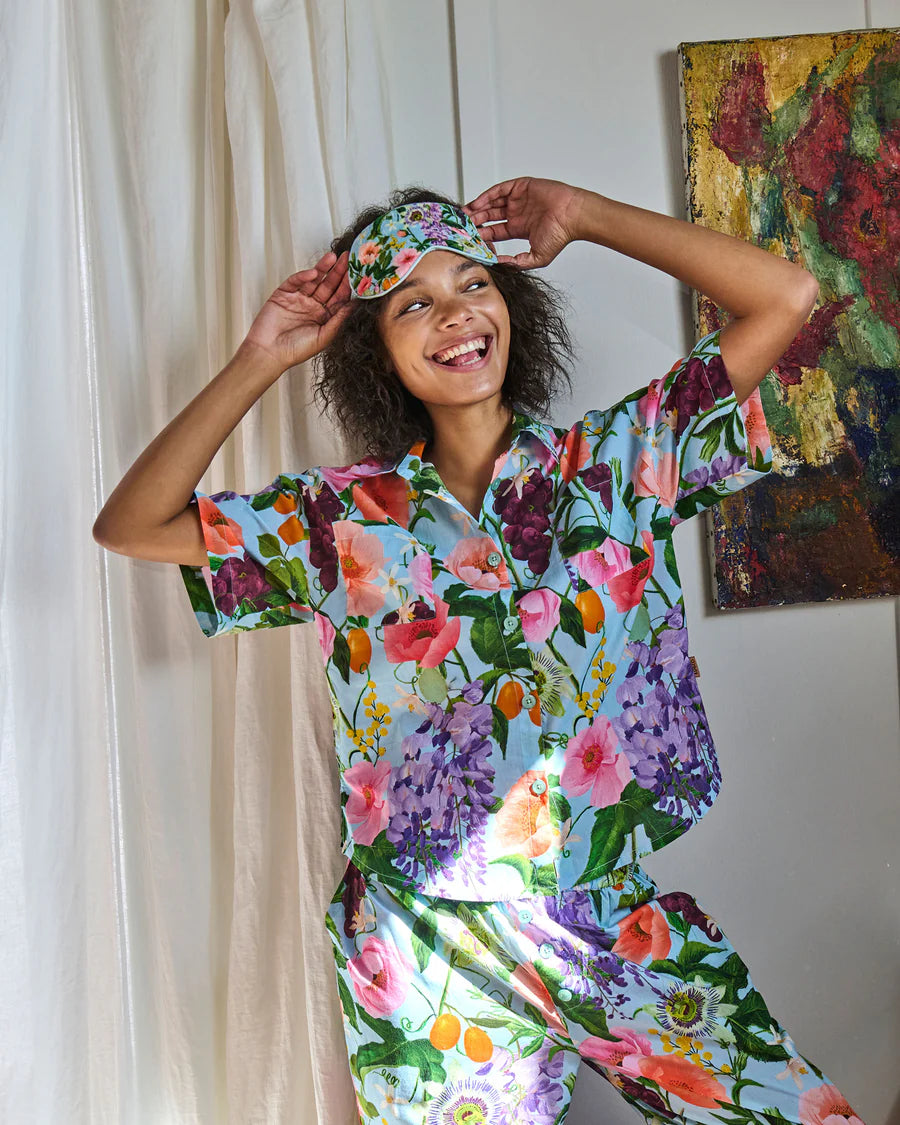 Woman wearing a colorful floral pajama set with a headband, standing in a room with a painting in the background.