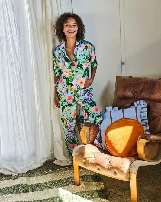 Woman in a floral pajama set standing next to a wooden chair with colorful cushions.