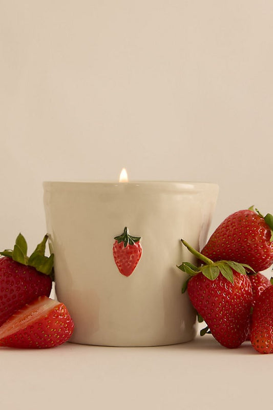 Candle with strawberry design surrounded by real strawberries on a neutral background