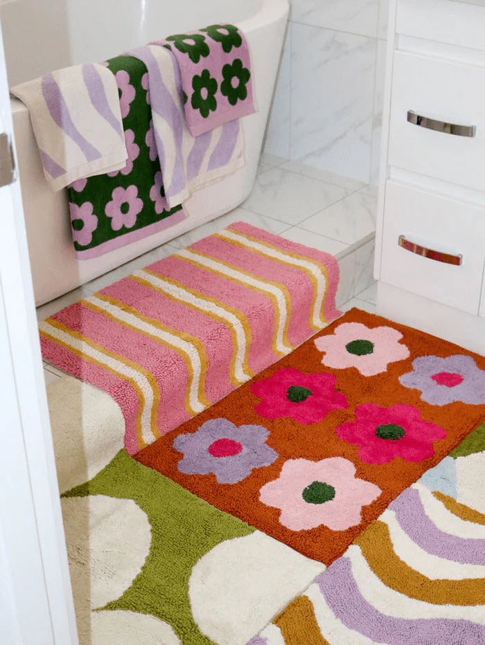 Colorful floral-patterned rug on a bathroom floor with towels hanging above.