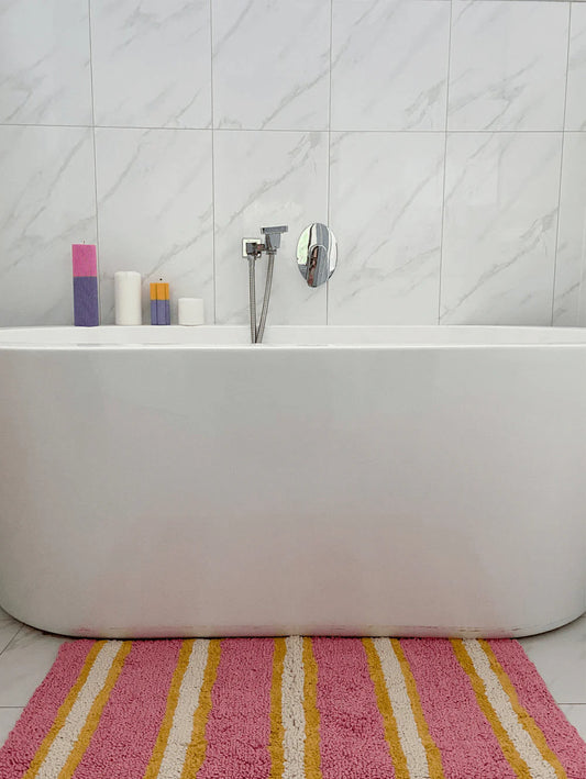 Bathroom with a bathtub and striped bath mat on a white tiled floor