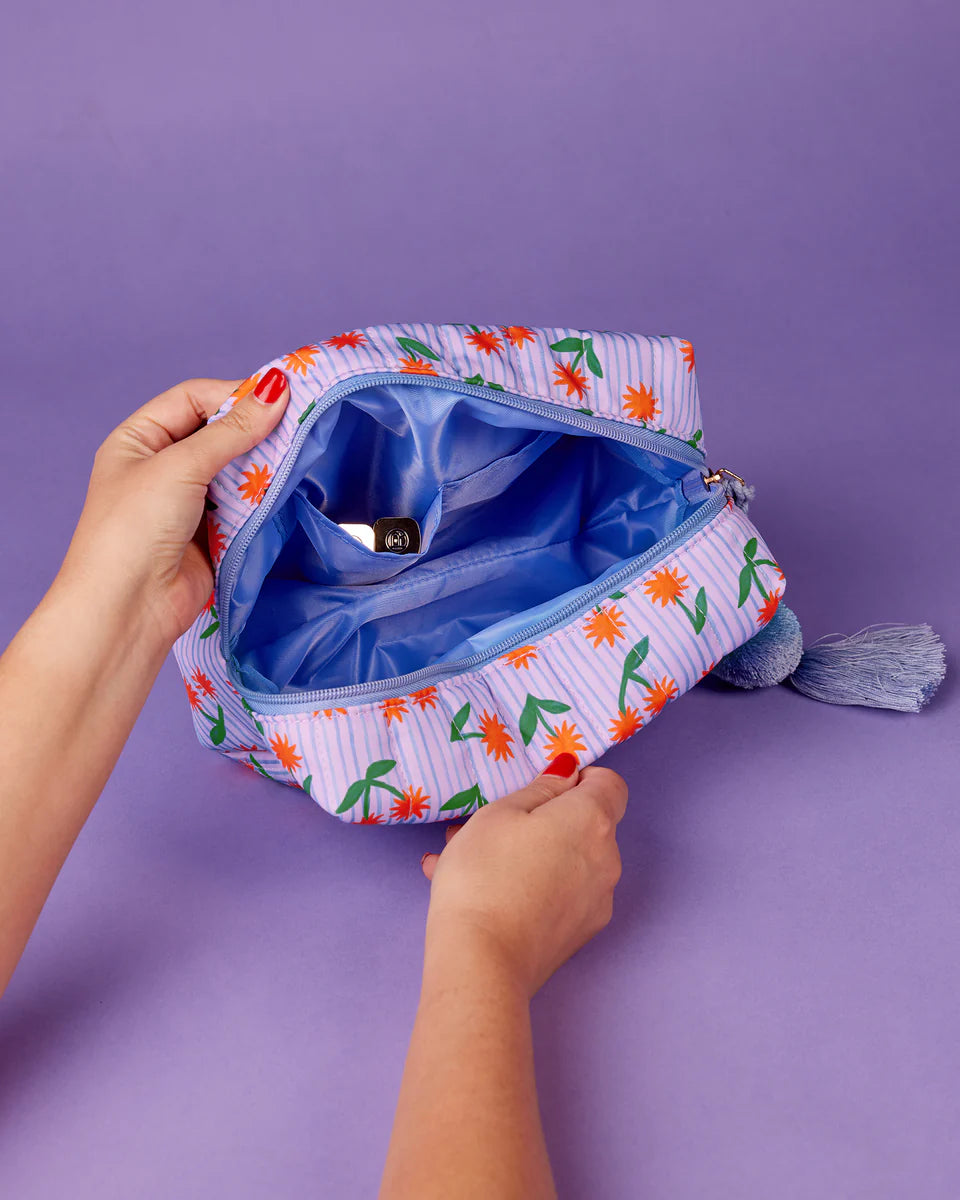 Hand holding a small pouch with floral pattern against a purple background