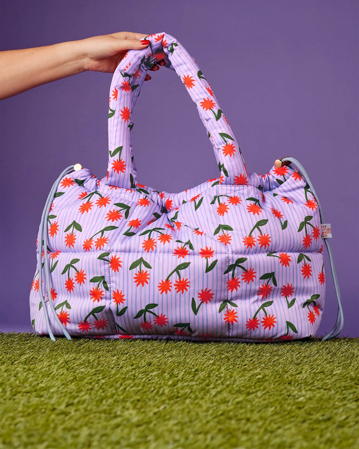 Floral patterned bag held by a hand on a purple and green background