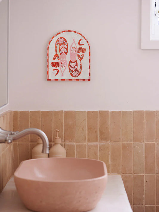 Bathroom with a pink sink and decorative wall art on a light pink wall.