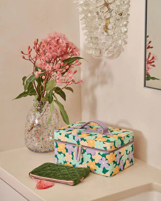Toiletry case sits on vanity next to vase and australian native pink flowers in vase. Green velvet toiletry bag lays in front of case.