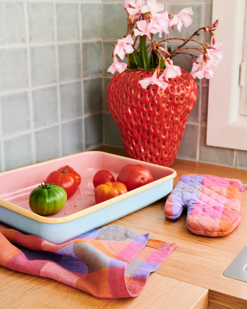 Kitchen corner features strawberry vase filled with blossom flowers, oven tray filled with tomatoes, laid on top of tea towel and oven mitt sat close by.