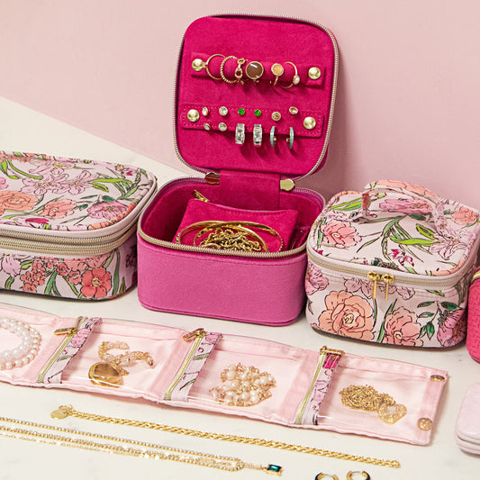 Pink jewelry case with floral design, jewelry inside, and accessories on a pink background