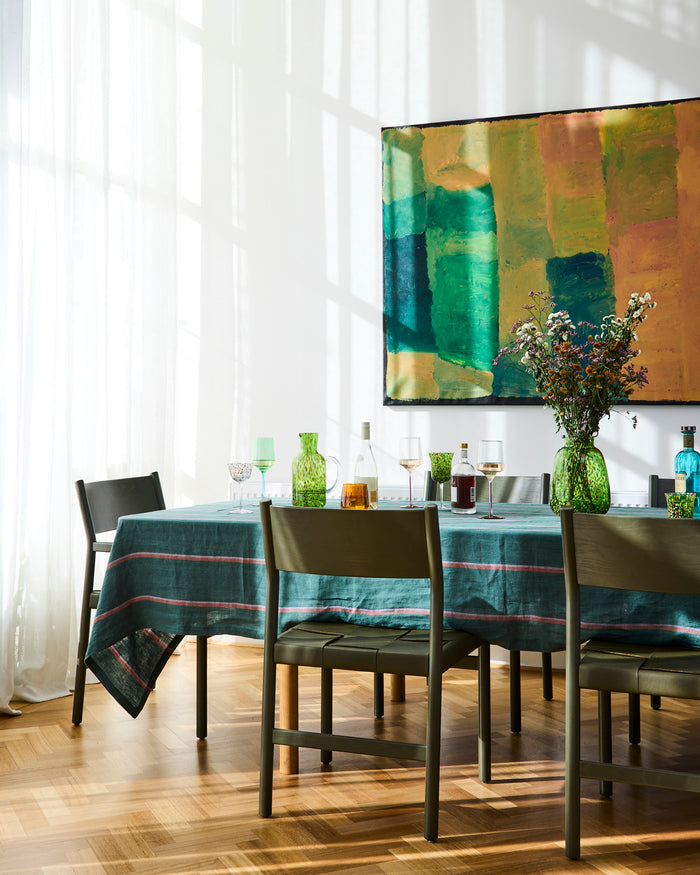Dining room with a tablecloth, chairs, and a colorful abstract painting on the wall.