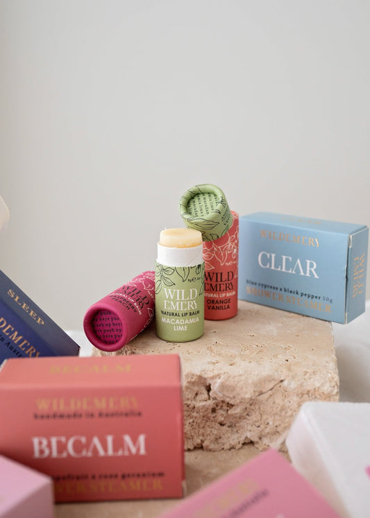 Collection of natural lip balms and shower steamers on a textured surface with a neutral background. Wild Emery Branding.