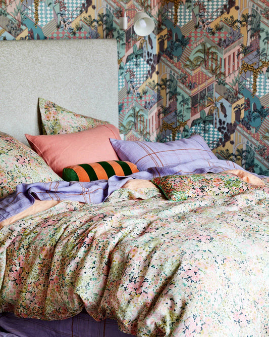 Bed styled with youre beautiful quilt cover from kip and co, assorted lilac and matching floral cushions. Including a bolster cushion in peach and khaki. Cream bed head and wallpaper geometric on wall behind bed.