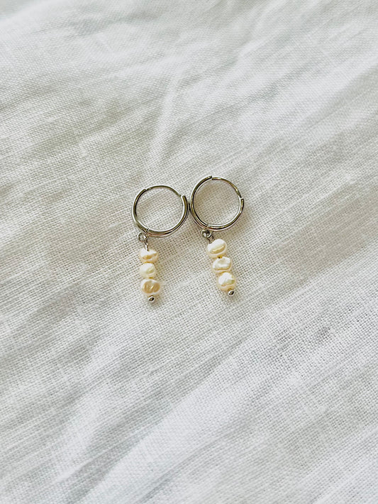 Pair of hoop earrings with pearl drops on a light fabric background