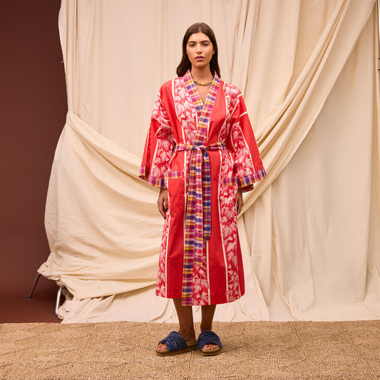 Woman wearing a red patterned dress standing in front of beige curtains.