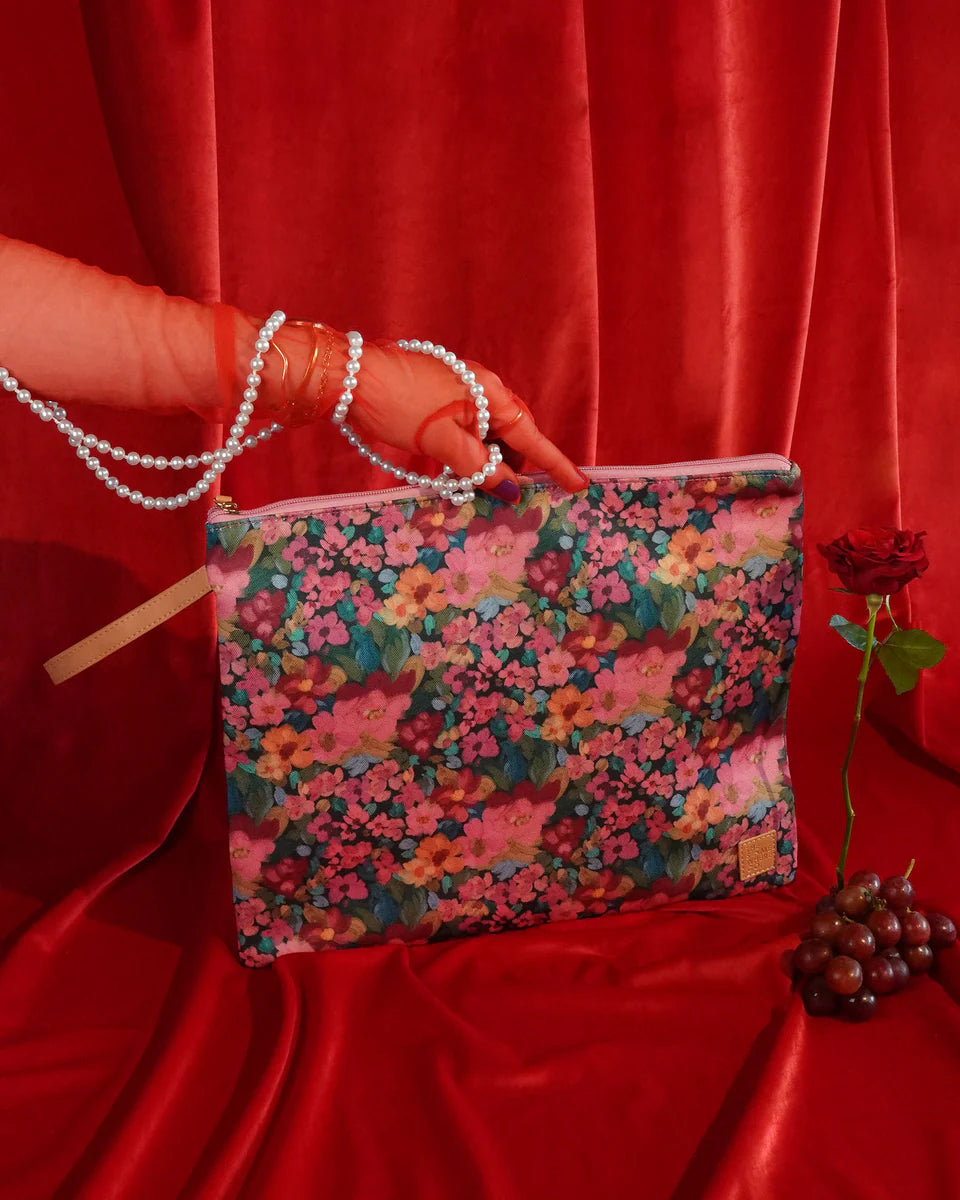 Floral-patterned pouch held by a hand against a red curtain background