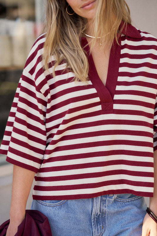 A woman wearing a cropped short-sleeve polo shirt with horizontal burgundy and off-white stripes, paired with light blue jeans.