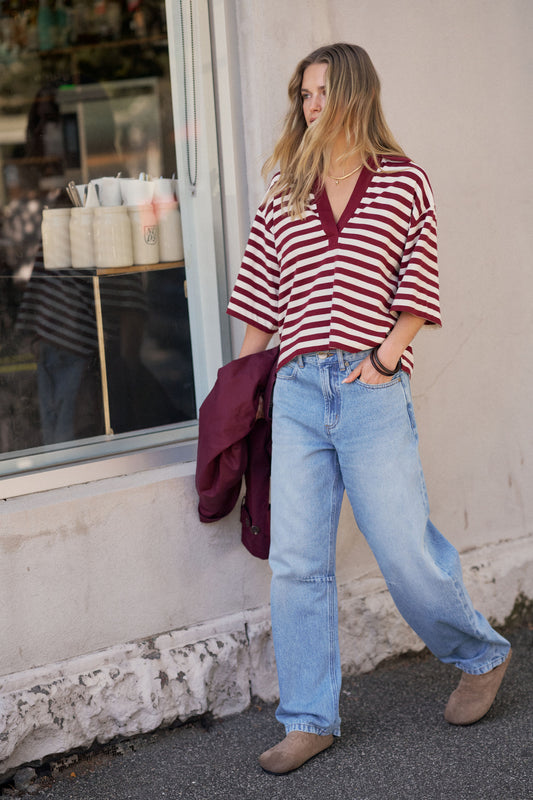 Woman wearing a red and white striped shirt and blue jeans standing in front of a store window.
