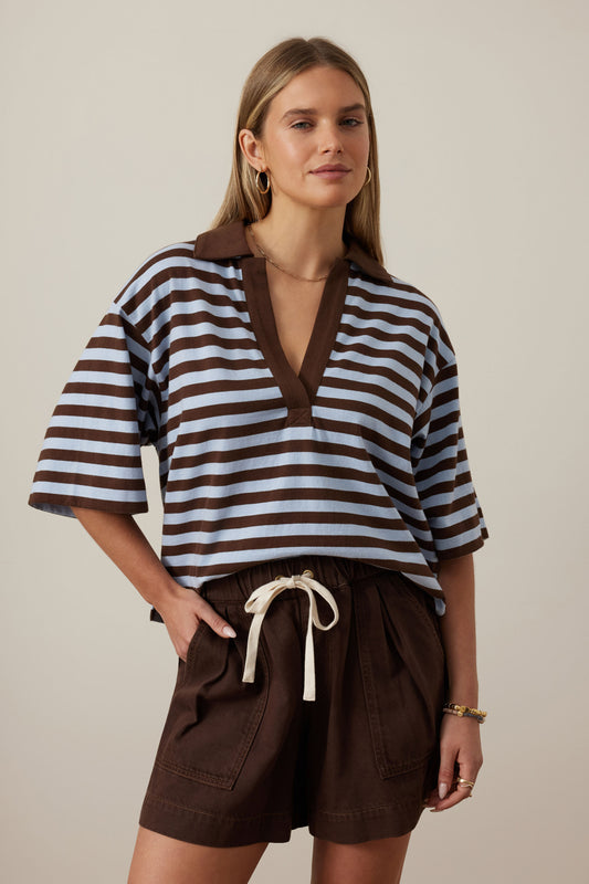 Woman wearing a brown and white striped shirt with brown shorts on a beige background
