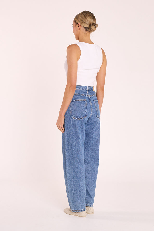 Person wearing blue jeans and a white top on a plain background