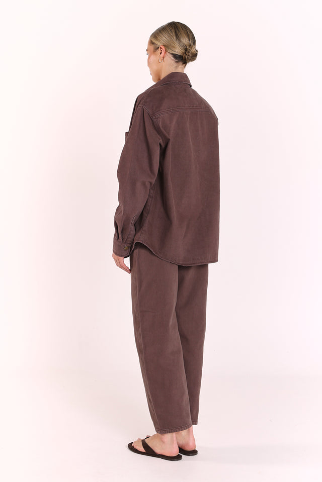 A model shown from the back wearing a matching dark brown corduroy shirt and trousers set, standing against a plain off-white studio background.