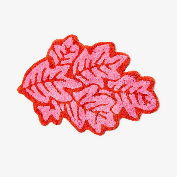 Pink and red leaf-shaped bath mat on a white background.