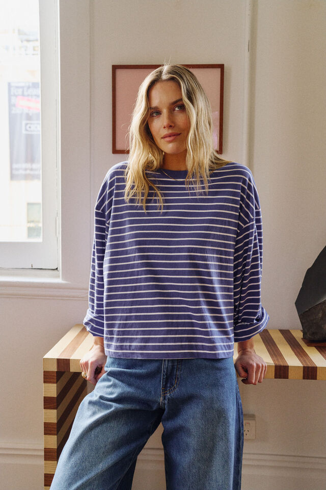 Woman wearing a blue and white striped shirt and jeans standing in a room with a window and wall art.
