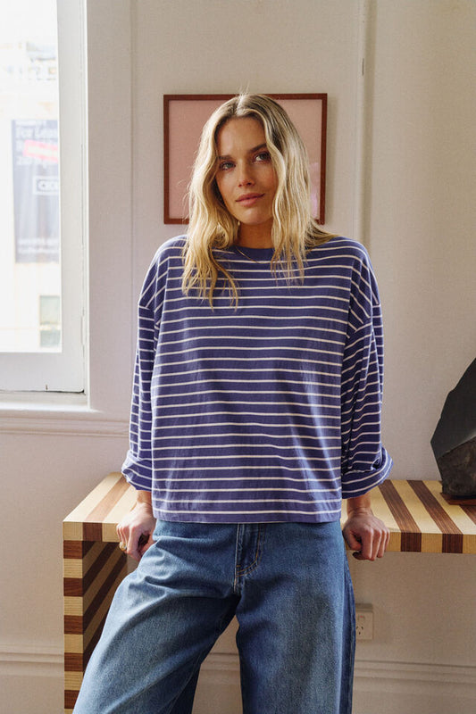 Woman wearing a blue and white striped shirt and jeans standing in a room with a window and wall art.