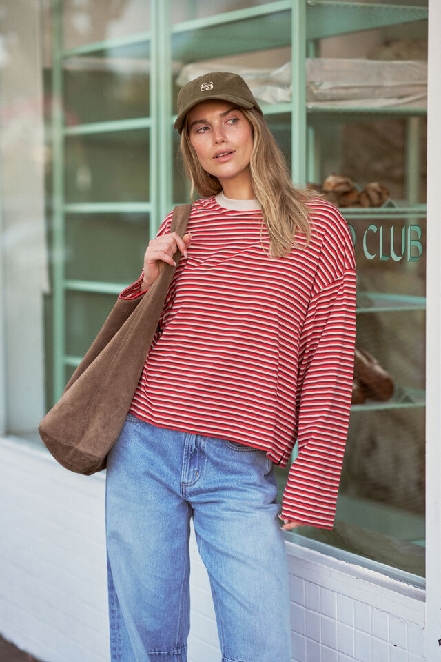 Woman wearing a red striped shirt and blue jeans, holding a brown bag, standing in front of a store window.